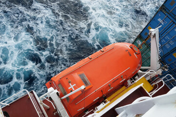 Orange colour life boat with reflective tape stickers observed from top secured with davits and...