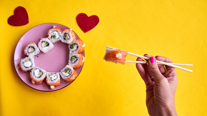 Sushi set in the shape of a heart on yellow background. Valentine day or March 8th food concept.The...