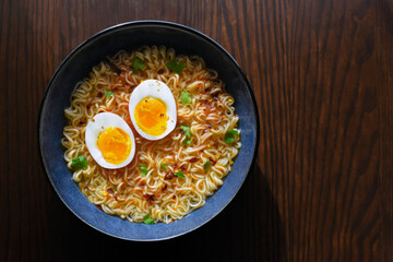 Instant noodles with boiled egg, chillies, coriander and seasoning.  Spicy noodles soup in a blue bowl.  Flat lay top view food photo.  Copy space is on the right side. 