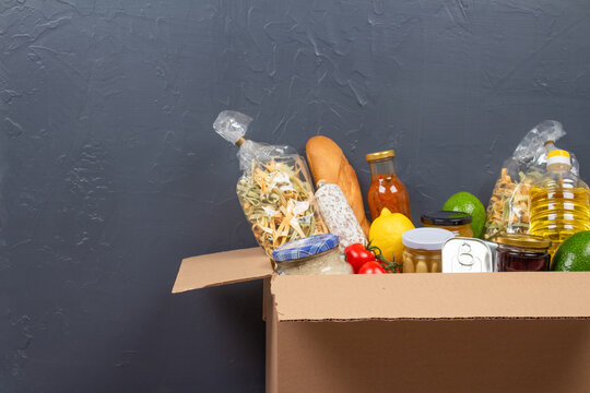Closeup view of donation box with different food donations on gray wall background with copy space - pasta, fresh vegatables, canned food, baguette, cooking oil. Food bank, food delivery concept