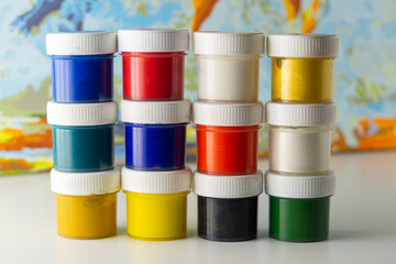 Set of gouache paint pots of different colors. Jars of multicolored paints on a blurred watercolor background. Creative hobby. Crafts and DIY
