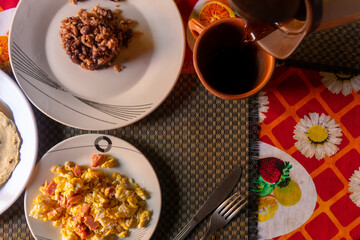 Topview Traditional Latin American breakfast, eggs with sausage and rice with beans and serving a cup of coffee.