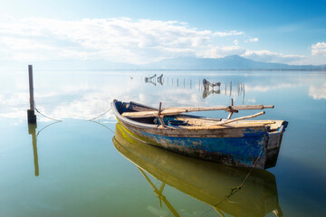 Close up of a small fishing boat. Reflection on the sea water of a small boat. Flat and calm sea reflecting the sky.