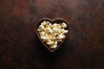 Popcorn in a brown wooden plate in the shape of a heart on a wooden table. 
