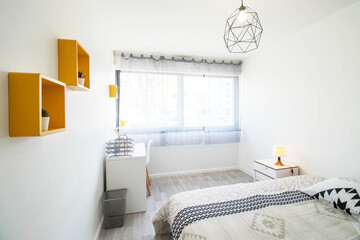 student room with bed and desk. Yellow frame on the wall. White bedside table. Windows