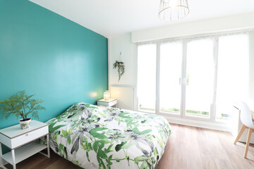 Room with green wall. Bedside table with lamp. White chair.