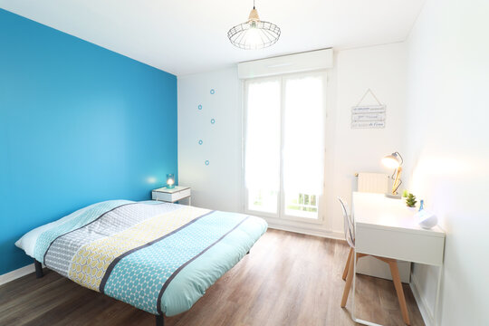 Bedroom with blue wall, seaside spirit. A desk and a transparent chair