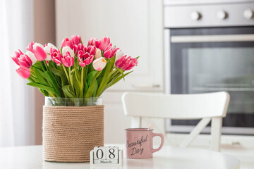 A bouquet of tulips on a white table. In the background, the interior of a white kitchen in the Scandinavian style. The concept of home comfort.The concept of International Women's Day on March 8.