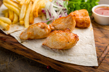 chicken kebab on board with french fries, onion and tomato sauce close up