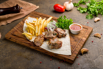 Kebab of pork with french fries, red onion and tomato sauce on the board