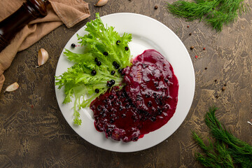 meat with black currant sauce on white plate top view