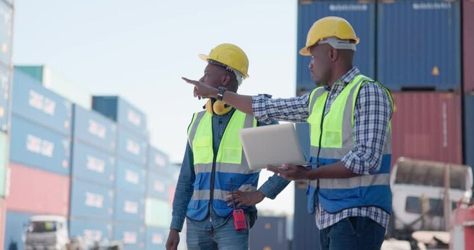 In front of a large industrial harbor with cargo background, two engineer male worker dockers in checking examine discussion with laptop.