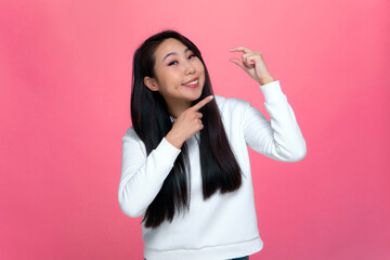 Happy asian young girl showing with fingers small price little size gesture on pink background....