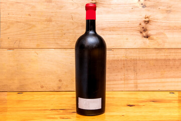 Bottle of red wine without signs in gold color and wooden background