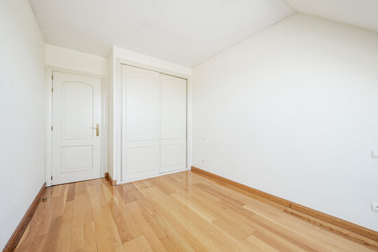 Room with white lacquered wood carpentry in wardrobe sliding doors and oak parquet floors
