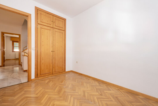 Empty room with built-in pine wood wardrobe and oak parquet floors