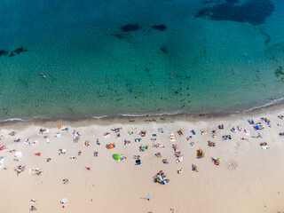 The beach is filled with vacationers by the sea. Top view from drone.
