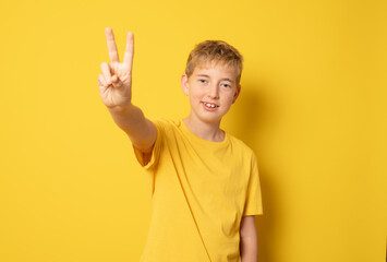 Smiling boy showing peace symbol isolated over yellow background.