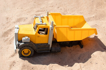 Yellow toy truck in sand lit by sunlight