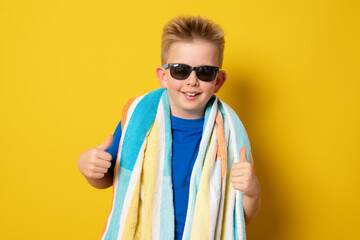 Cute boy wearing sunglasses in summer outfit standing with thumbs up over yellow background.