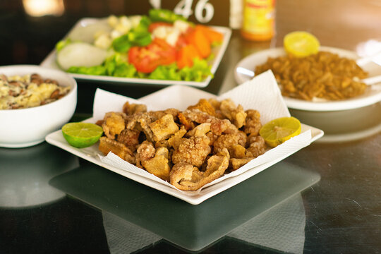 fried pork crackling,
traditional Brazilian recipe for pork crackling on a table with salad and a portion of rice in the background