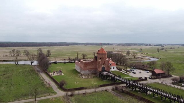Aerial view of brick old tower with flag. Behind the tower there is a river. Place for historical tourism. Aerial View of Liw Castle in Poland.