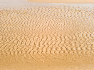 Golden sand textured by wind and sea water during the Golden Hour at Itacoatiara beach. Selective focus.