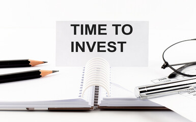 Text TIME TO INVEST on paper card,pen, pencils, glasses,financial documentation on table - business concept