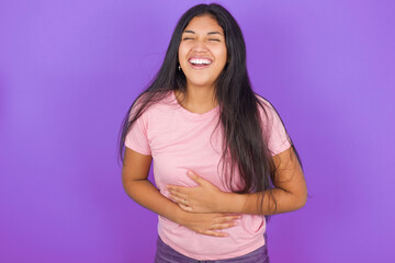 Obraz premium Hispanic brunette girl wearing pink t-shirt over purple background smiling and laughing hard out loud because funny crazy joke with hands on body.