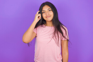Hispanic brunette girl wearing pink t-shirt over purple background tries to memorize something,...