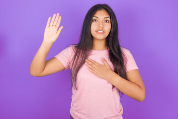 Hispanic brunette girl wearing pink t-shirt over purple background Swearing with hand on chest and open palm, making a loyalty promise oath