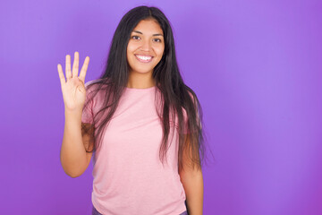 Hispanic brunette girl wearing pink t-shirt over purple background showing and pointing up with fingers number four while smiling confident and happy.