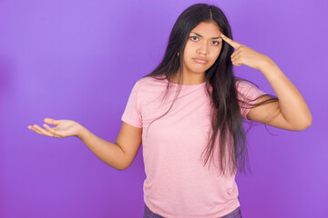 Hispanic brunette girl wearing pink t-shirt over purple background confused and annoyed with open...