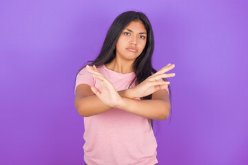Hispanic brunette girl wearing pink t-shirt over purple background Rejection expression crossing arms doing negative sign, angry face