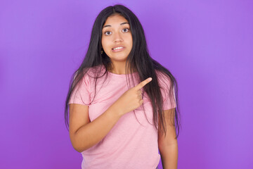 Hispanic brunette girl wearing pink t-shirt over purple background Pointing aside worried and...