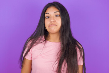 Hispanic brunette girl wearing pink t-shirt over purple background making grimace and crazy face,...