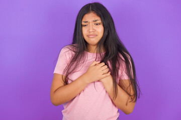 Obraz premium Sad Hispanic brunette girl wearing pink t-shirt over purple background desperate and depressed with tears on her eyes suffering pain and depression in sadness facial expression and emotion concept