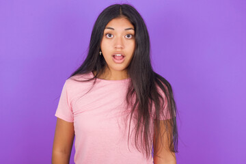 Fototapeta premium Oh my God. Surprised Hispanic brunette girl wearing pink t-shirt over purple background stares at camera with shocked expression exclaims with unexpectedness,