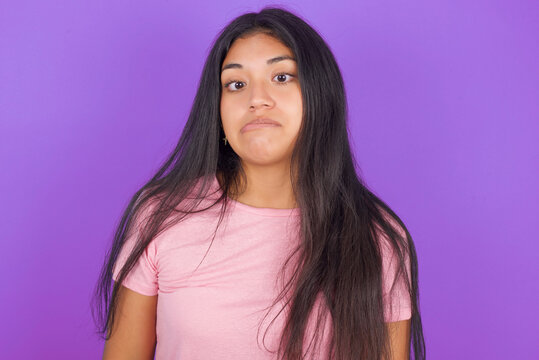 Hispanic brunette girl wearing pink t-shirt over purple background making grimace and crazy face, screaming out of control, funny lunatic expressing freedom and wild.