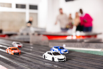 Cheerful and happy men and women play together with slot car racing track