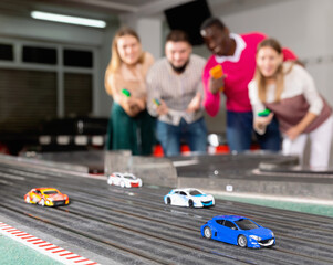 Slot car racing track. Emotional positive players drive toy cars in the background
