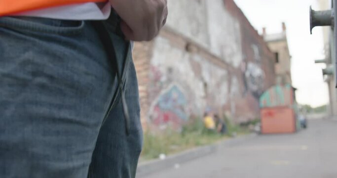 Vandal zips up the fly on jeans after peeing on the street in broad daylight, forgetting to fasten leather belt, then put his hands in pockets as if nothing had happened, close up.