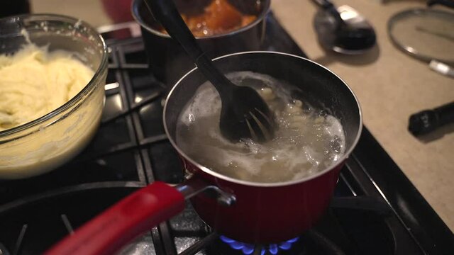 This Video Shows A Hand Stirring Elbow Macaroni In A Red Sauce Pan As It Boils On The Stove.