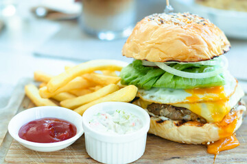 hamburger with french fries, ketchup, mustard and fresh vegetables on a cutting wooden board.