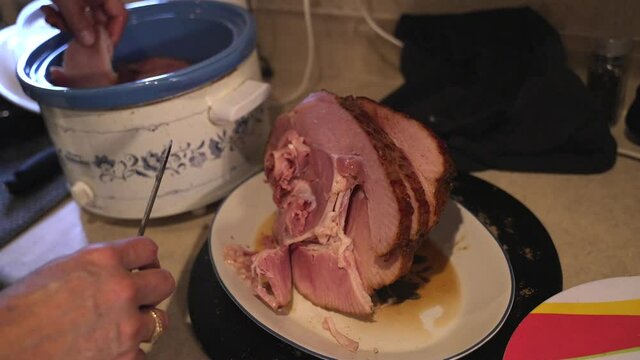 This video shows hands pulling and cutting home made baked ham and placing pieces of the fresh meat in a crockpot.