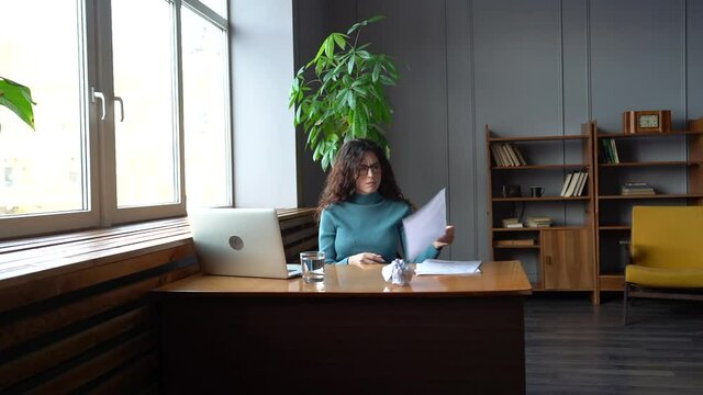 Stressed exhausted businesswoman feel tired after work with documents for report crumple paper sitting at office desk with laptop. Frustrated female specialist suffer from lack of ideas and motivation