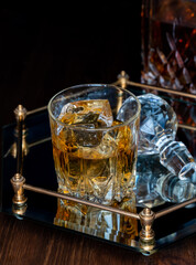 A glass of whiskey on a glass tray, against a black background.
