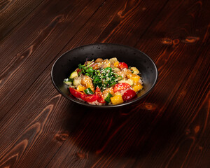 Salad of tomatoes, cucumbers, avocado, pineapple, scallop meat with sesame seeds in a plate on a dark wood background