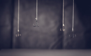 Fishing hooks hang on a dark background. Get hooked. Fall into the trap. Hook