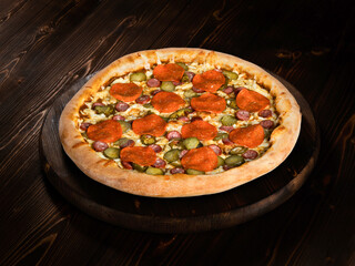 Food, Italian pizza with pepperoni salami, jalapeno hot pepper and cheese on a round wooden tray on a dark wood background